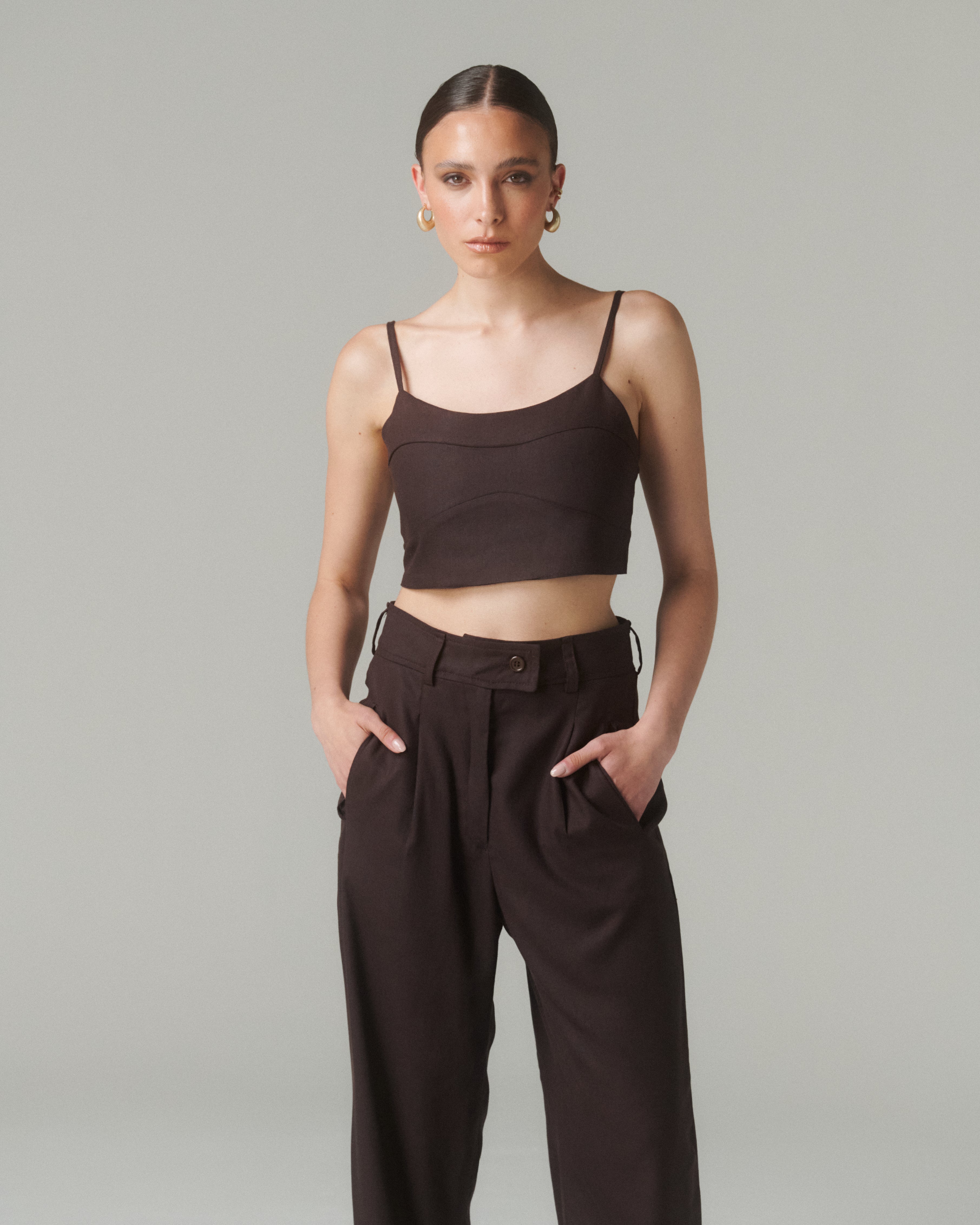 Modelo de pie, mostrando la parte superior de la blusa, enfoque en el escote recto y tirantes finos.  Fondo neutro o tono cálido.