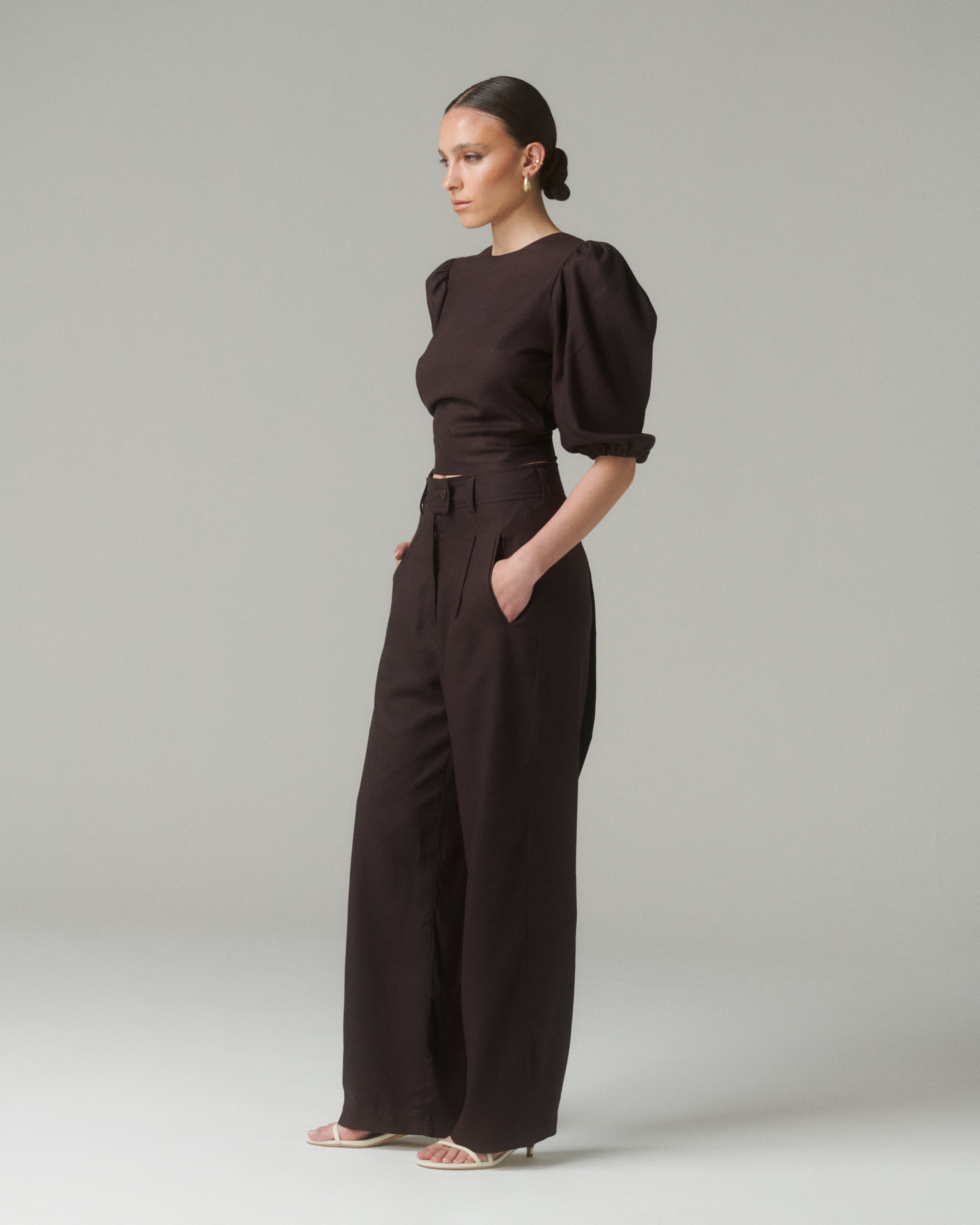 Vista lateral de cuerpo completo de la Blusa Aura Café con pantalones negros, mostrando elegancia y silueta definida.