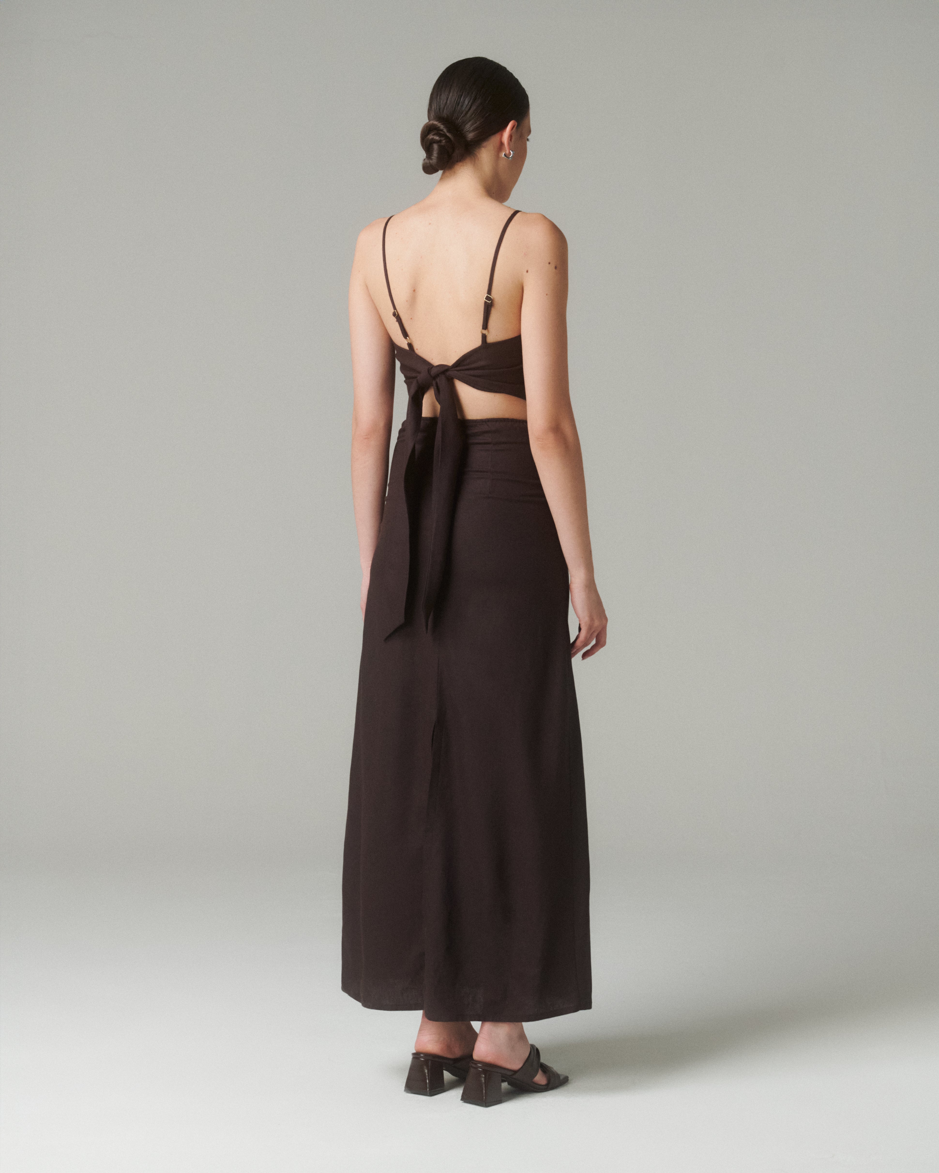 Mujer luciendo el Vestido Moa Café desde la espalda, destacando su diseño elegante y tirantes ajustables.