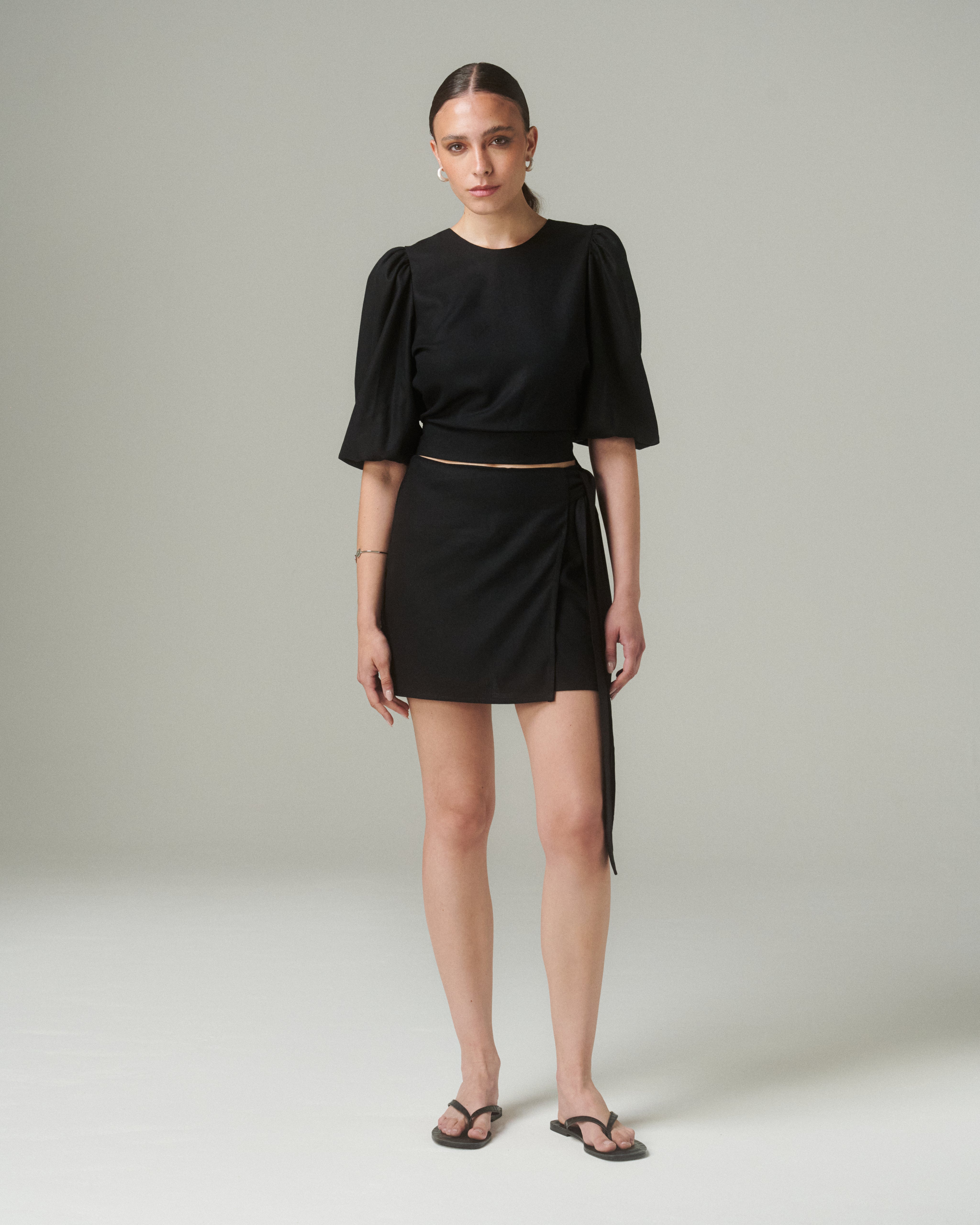 Vista frontal completa de la Blusa Aura Negro, mostrando el ajuste en la cintura y el diseño elegante, combinada con falda corta del mismo color.