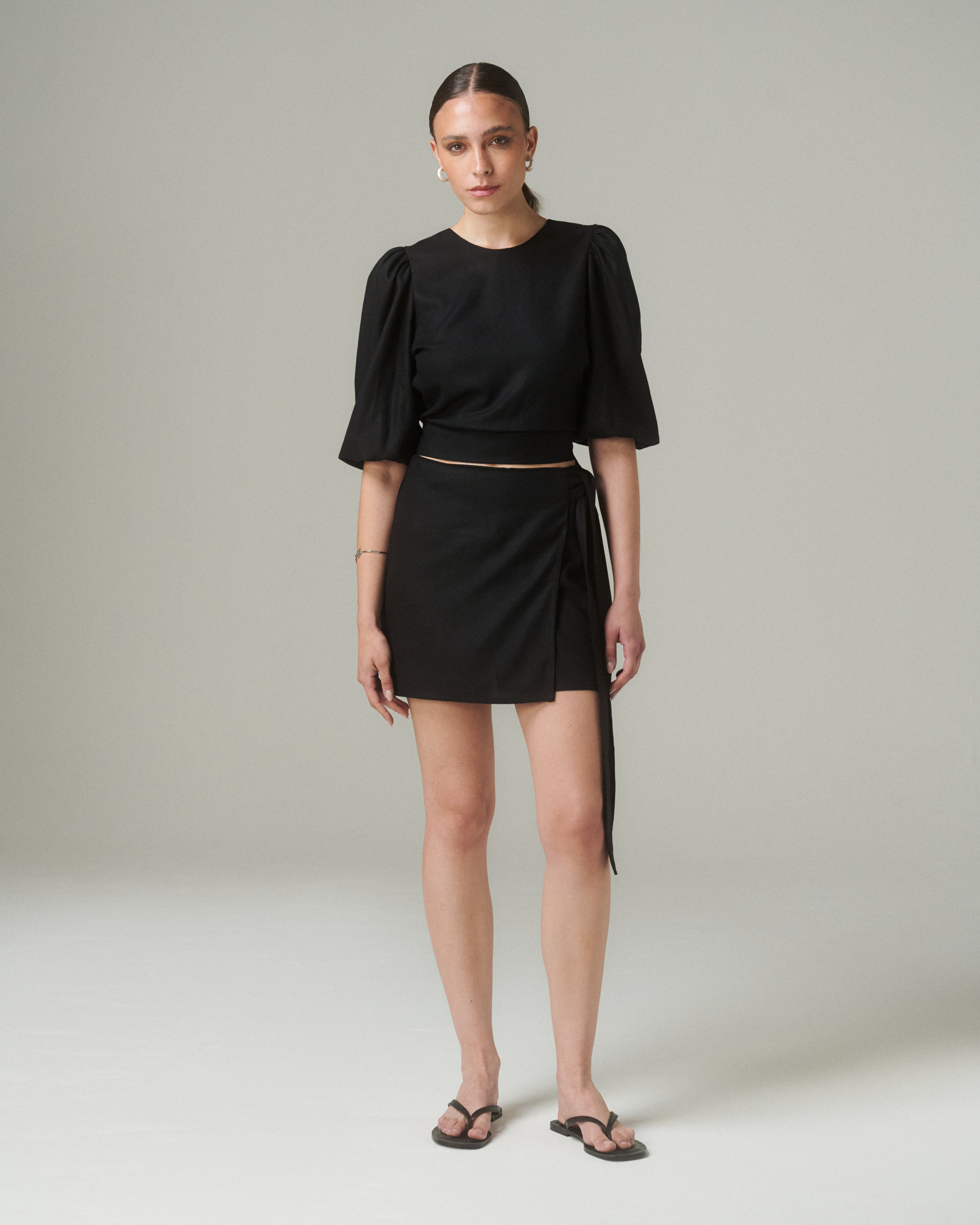 Vista frontal completa de la Blusa Aura Negro, mostrando el ajuste en la cintura y el diseño elegante, combinada con falda corta del mismo color.