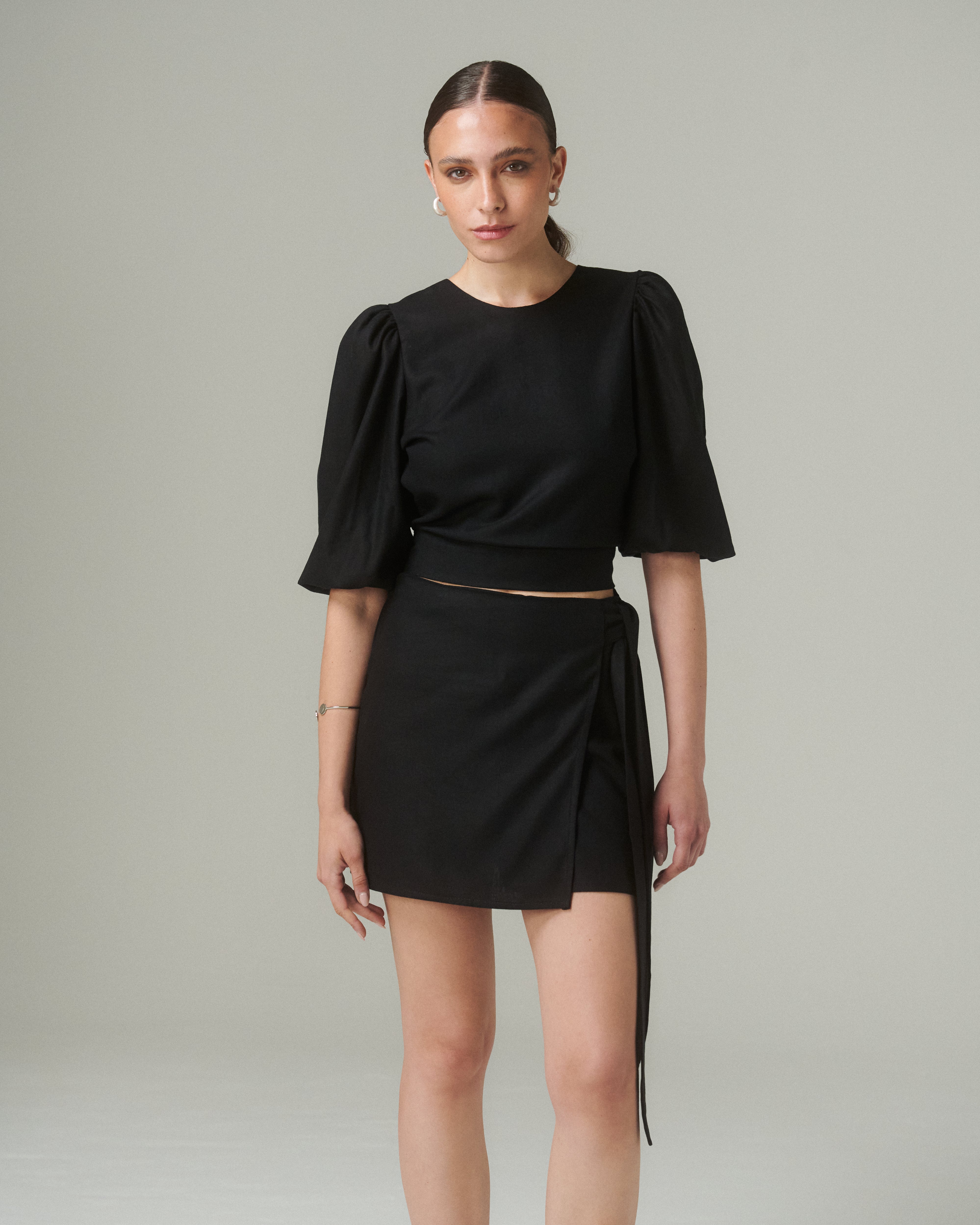 Mujer usando la Falda Lina Negro, prenda oscura con lazo lateral y silueta envolvente.