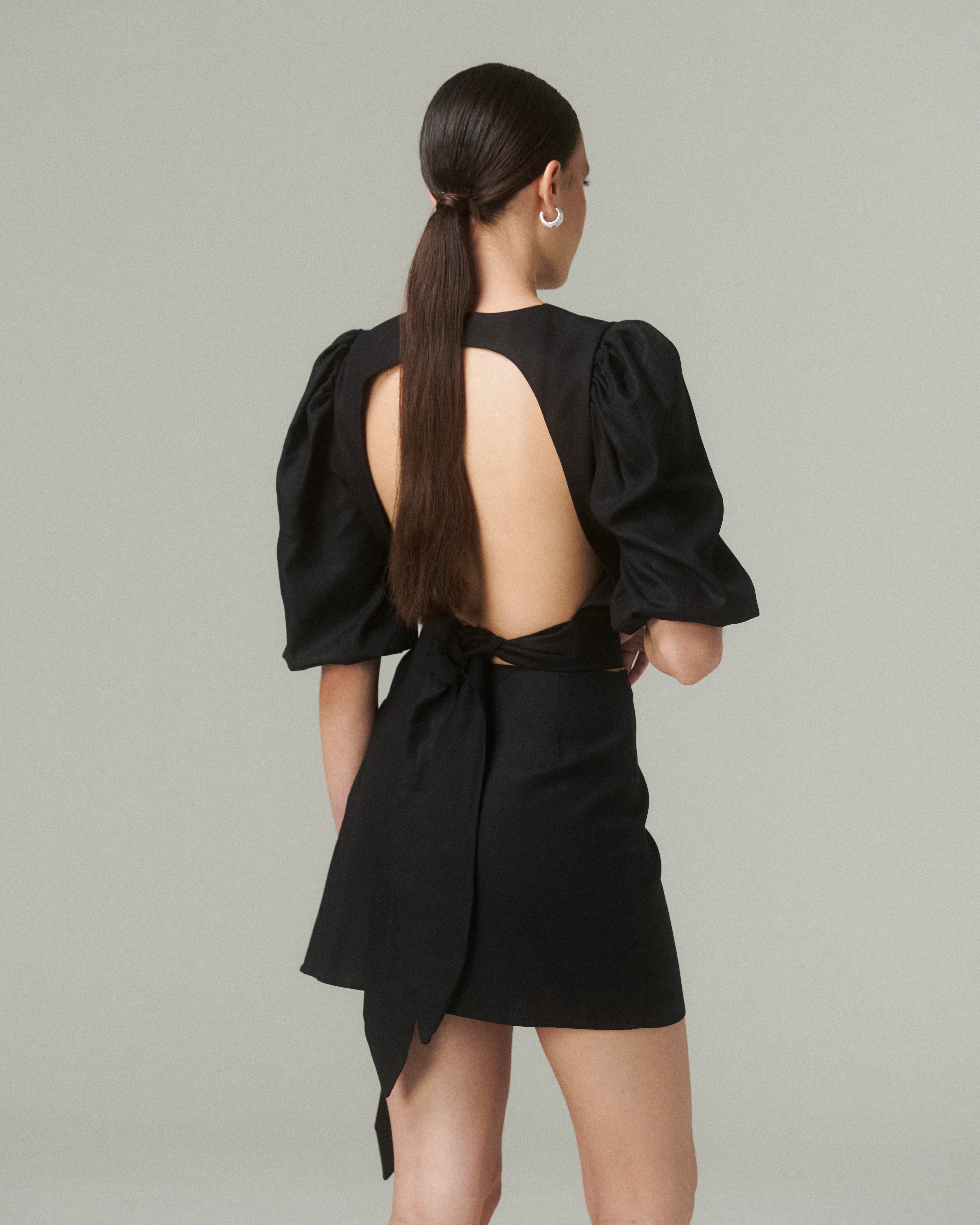 Mujer de espaldas mostrando la Falda Lina Negro con lazo lateral y detalles de diseño elegante.