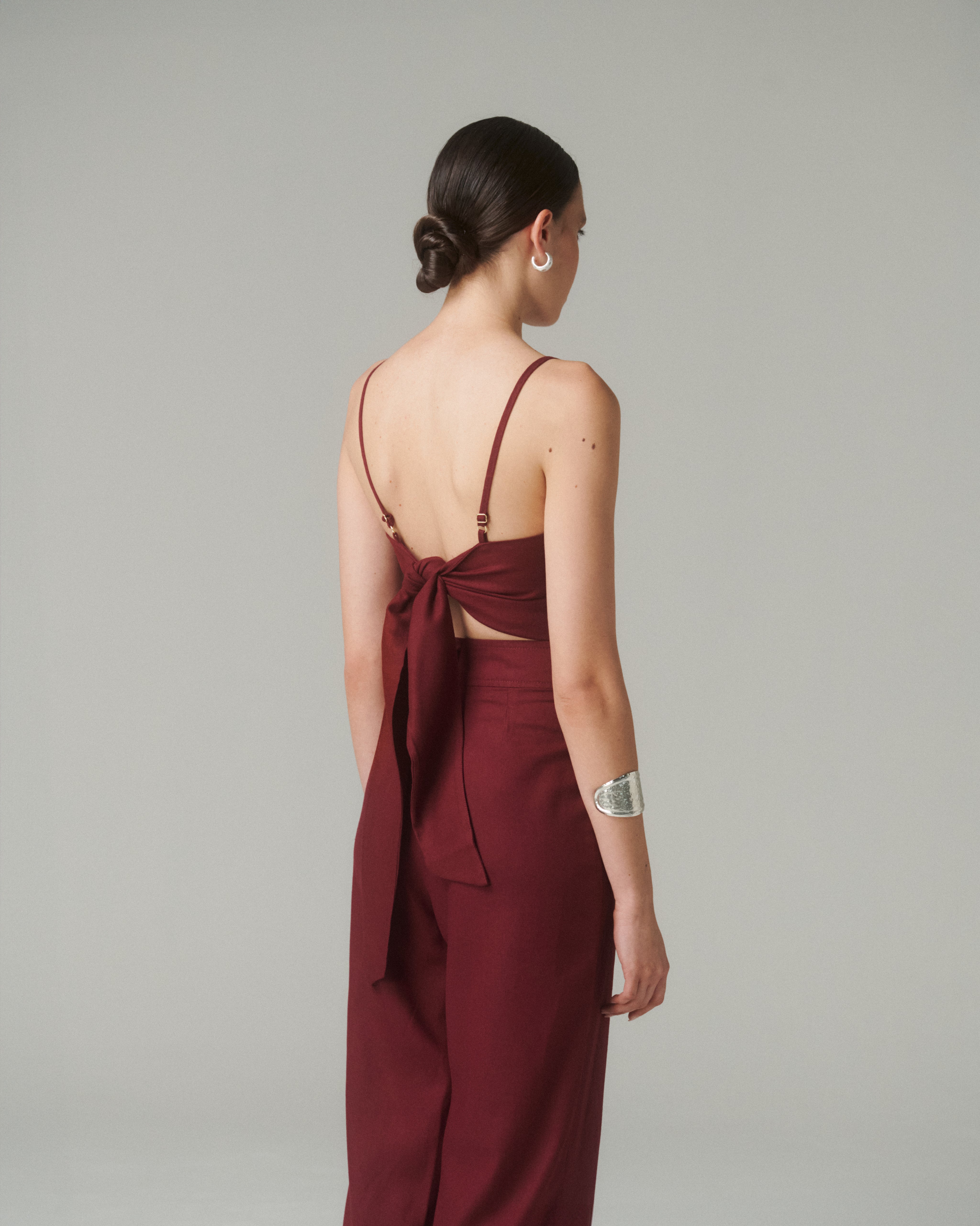 Mujer luciendo la Blusa Nina Burdeo con lazo ajustable en la espalda, destacando su diseño contemporáneo.