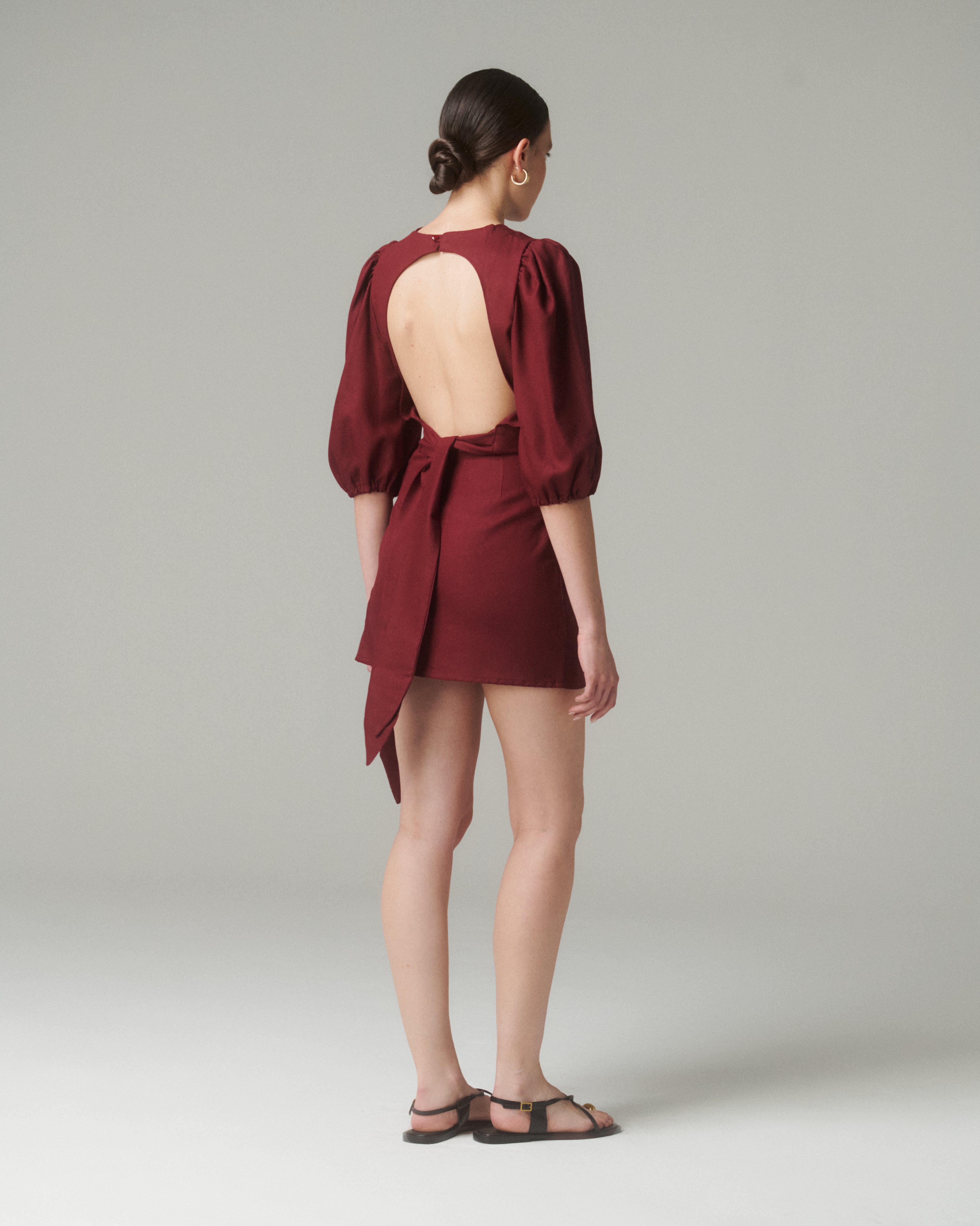 Vista trasera completa de la Blusa Aura Burdeo, combinada con falda corta del mismo color, mostrando el diseño general y caída de la prenda.