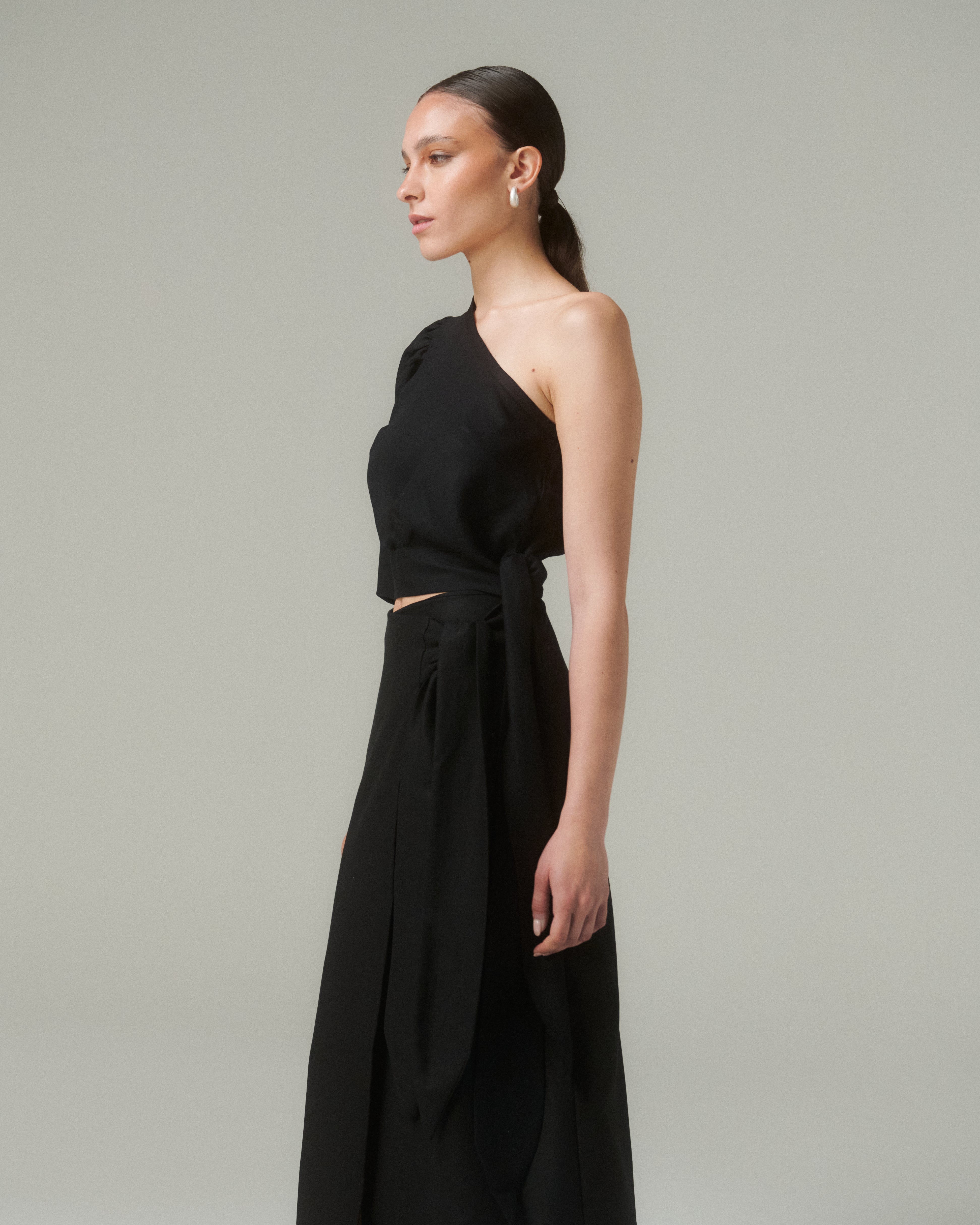 Blusa Bimba Negro model showcasing an asymmetric design, revealing one shoulder and featuring a side bow for a perfect fit.