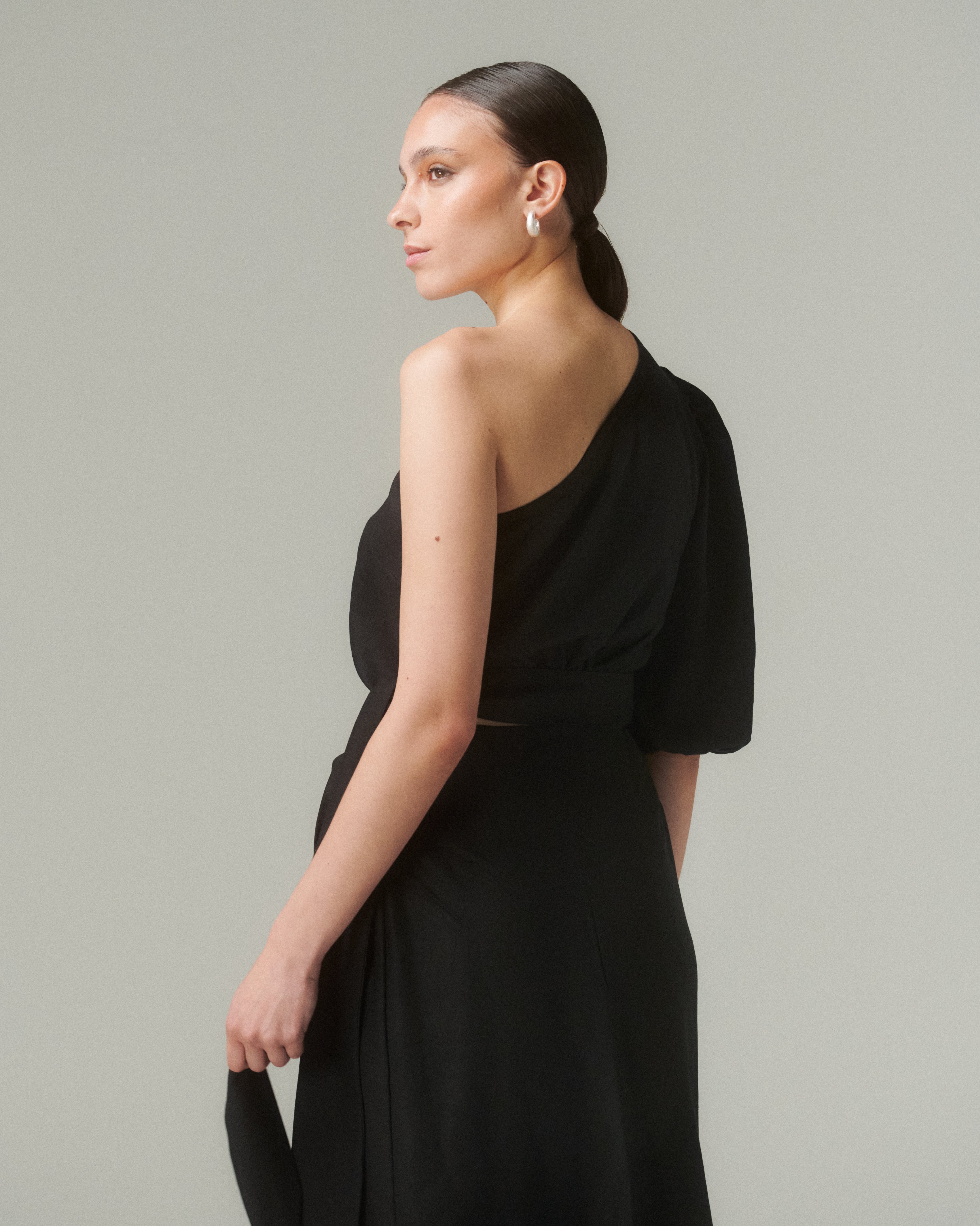 Model wearing Blusa Bimba Negro, showcasing asymmetrical design and one-shoulder detail.