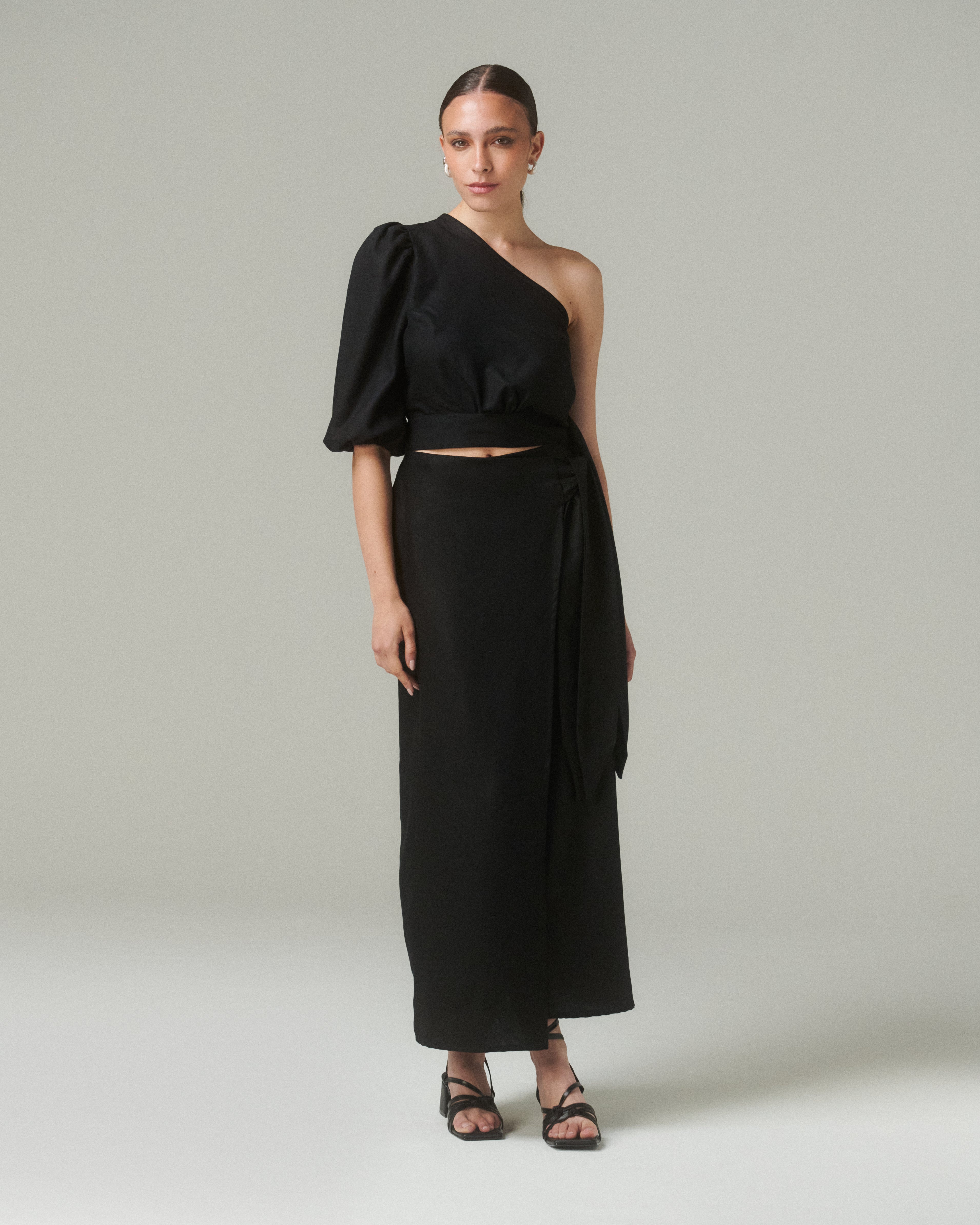 Model wearing Blusa Bimba Negro, an asymmetrical black blouse with puffed sleeve and side tie.