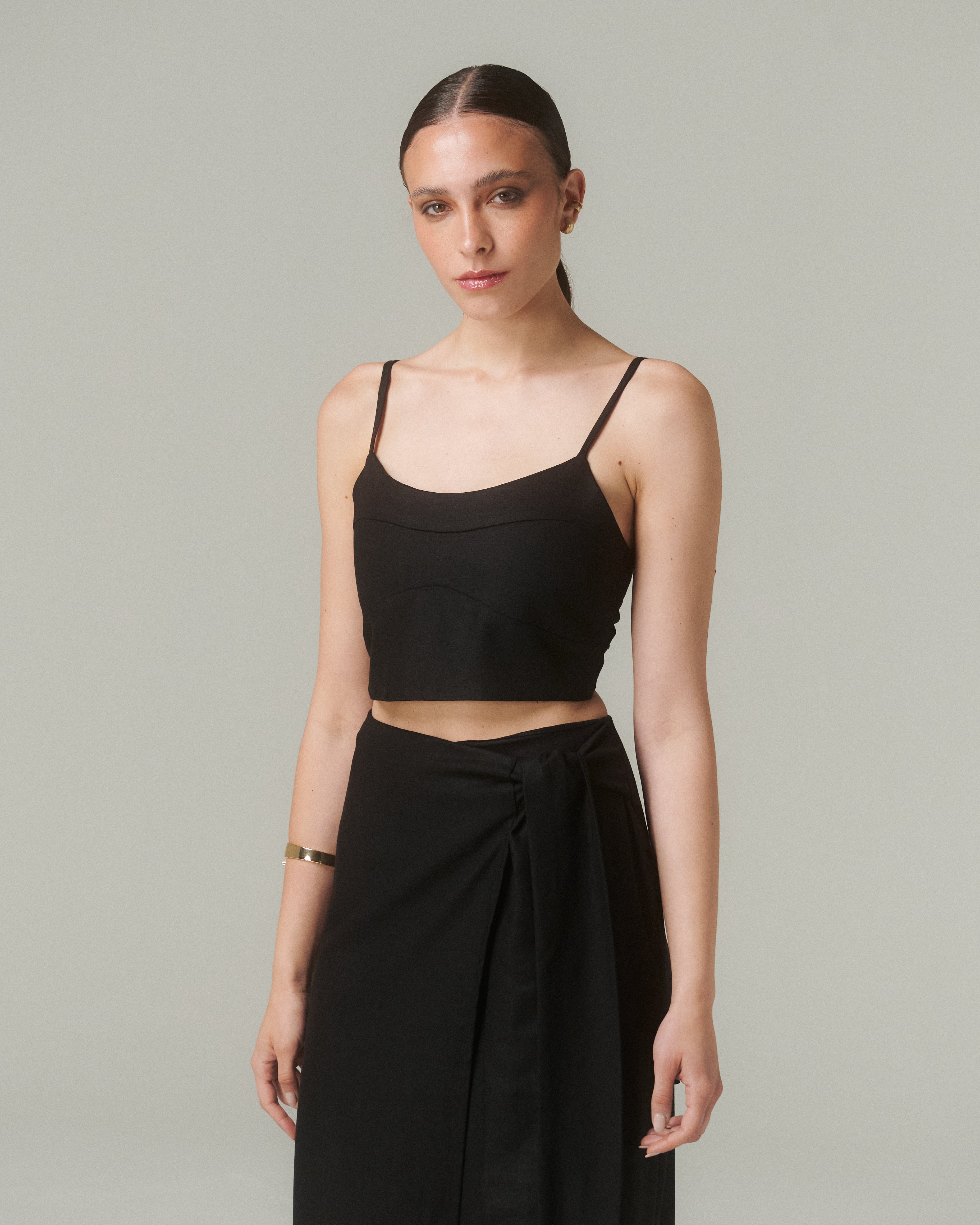 Modelo de pie, mostrando la parte superior de la blusa, enfoque en el escote recto y tirantes finos.  Fondo neutro o tono cálido.