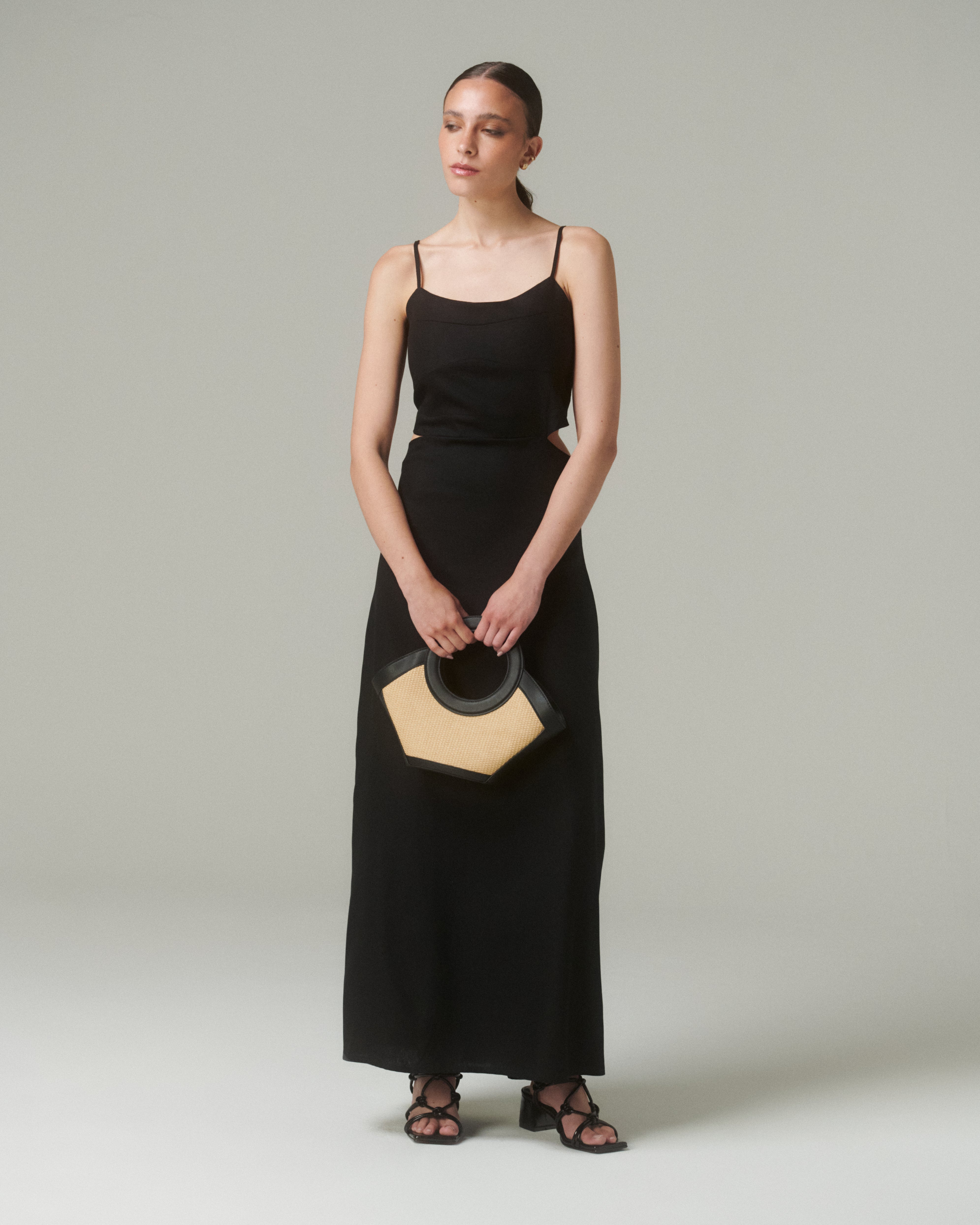 Modelo usando el Vestido Moa Negro con tirantes finos y bolso elegante en un fondo claro.