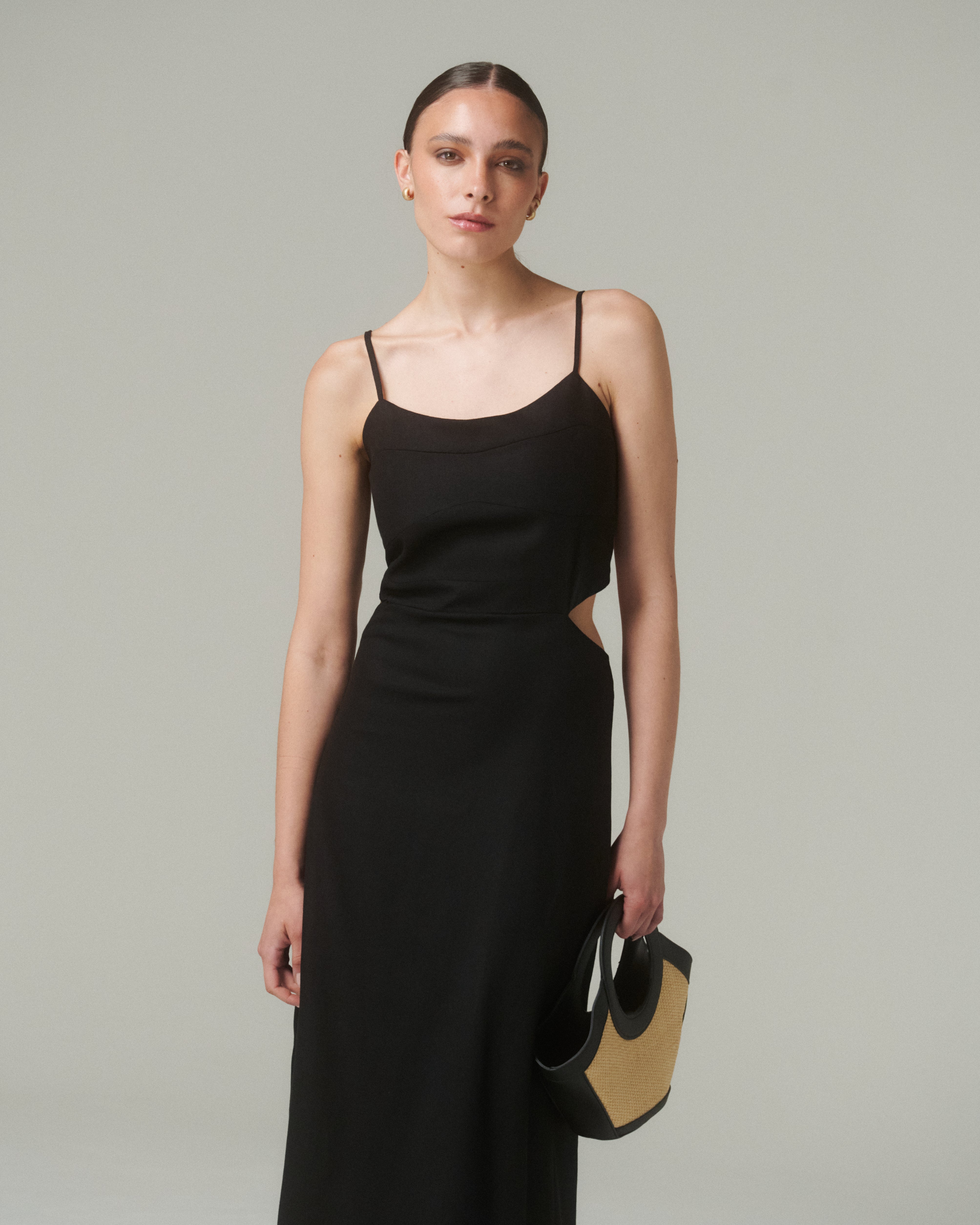 Modelo usando un Vestido Moa Negro, con tirantes finos y diseño ajustado, sosteniendo un bolso.