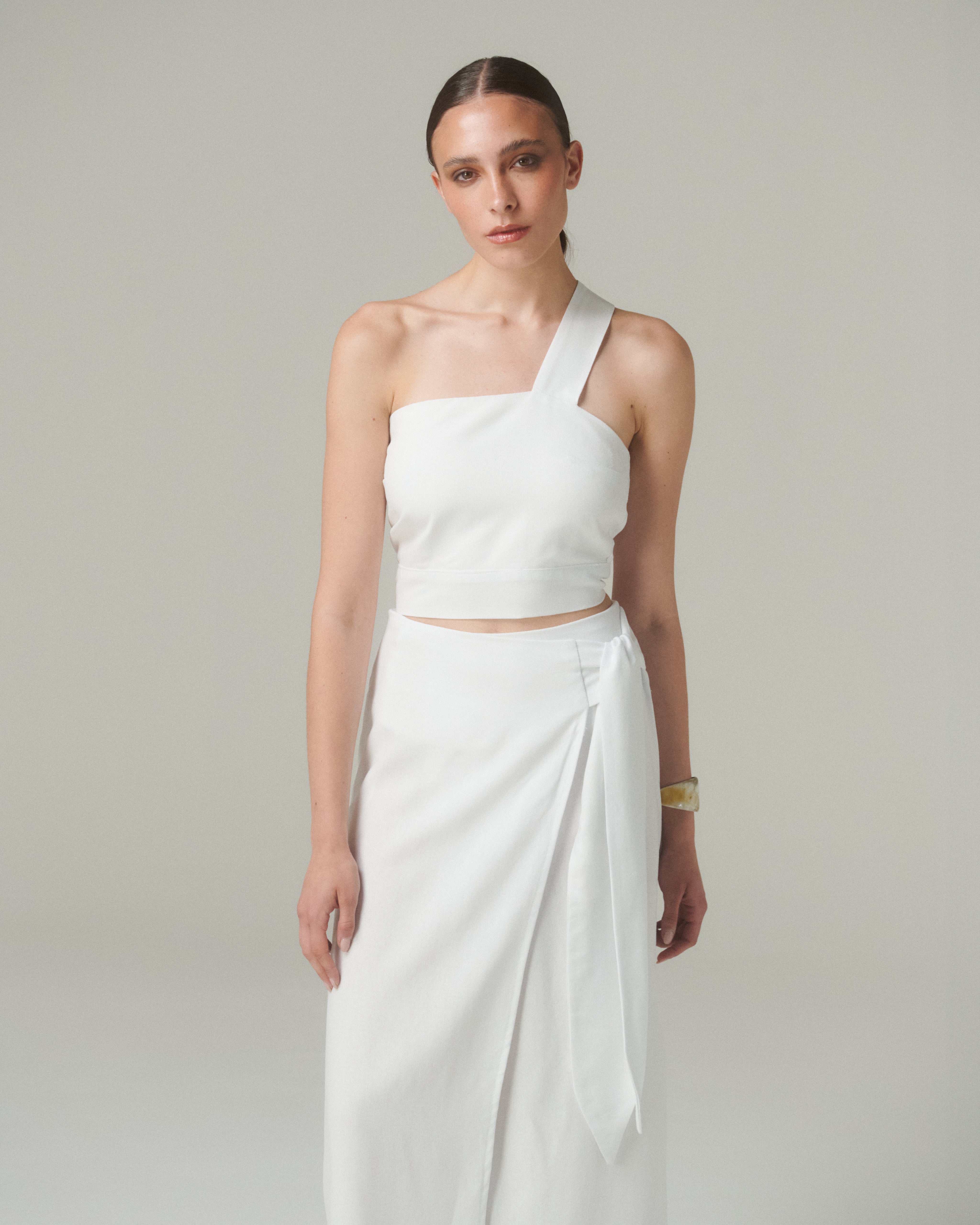 Modelo vistiendo Falda Lara Blanco con blusa blanca asimétrica, estilo elegante y moderno en fondo neutral.