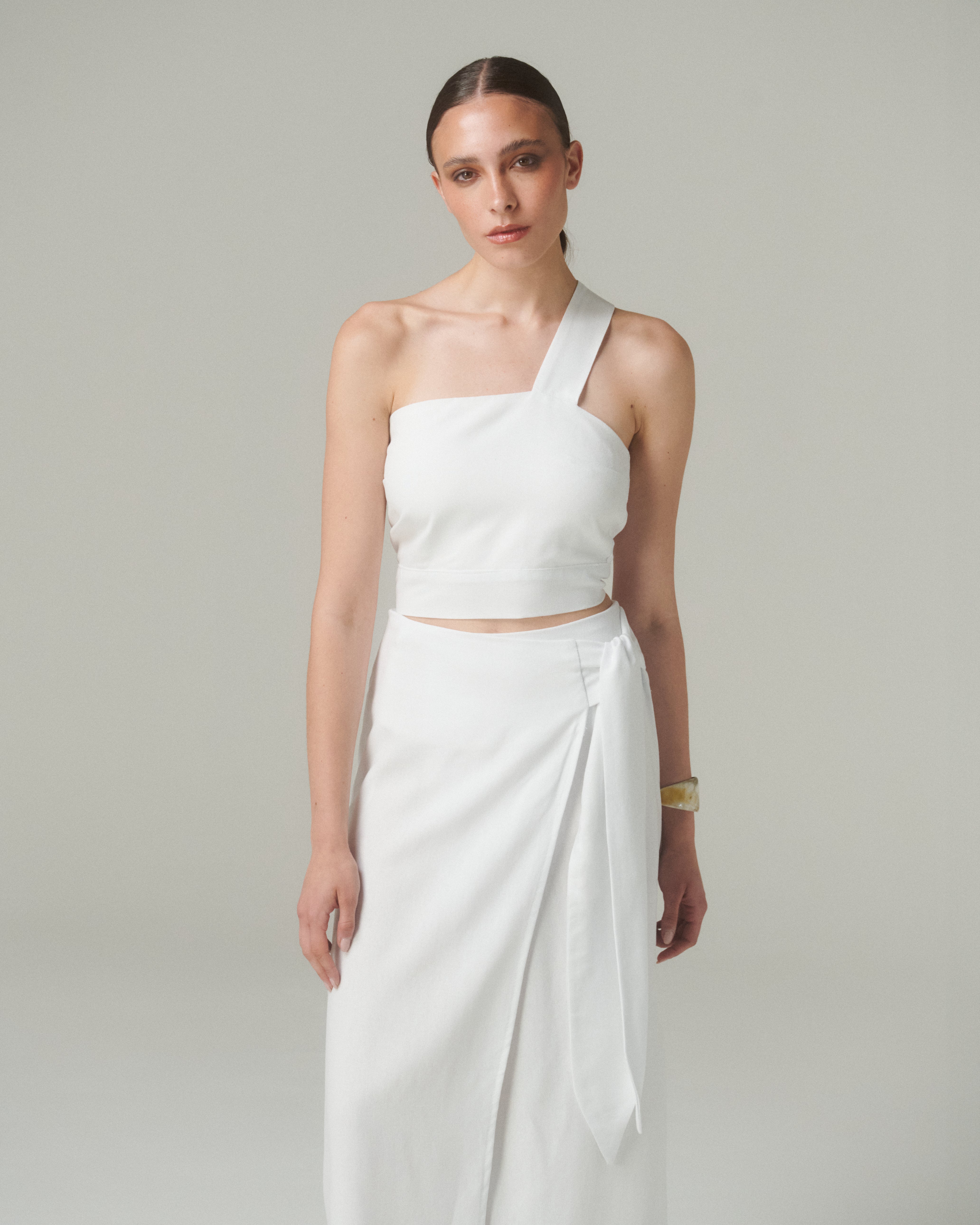 Modelo vistiendo Falda Lara Blanco con blusa blanca asimétrica, estilo elegante y moderno en fondo neutral.