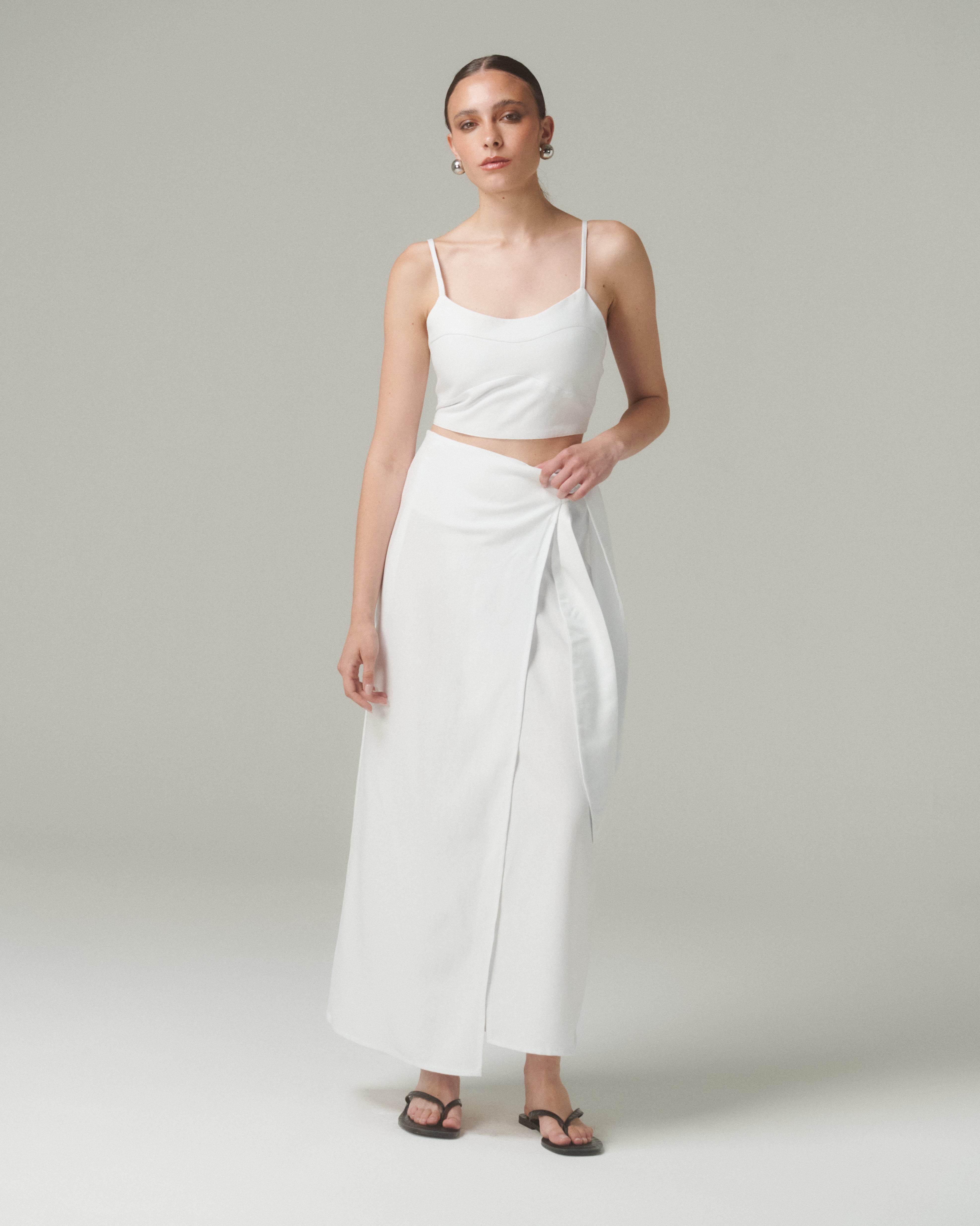 Mujer modelando la Blusa Nina Blanco, una blusa blanca con tirantes finos y lazo ajustable en la espalda.