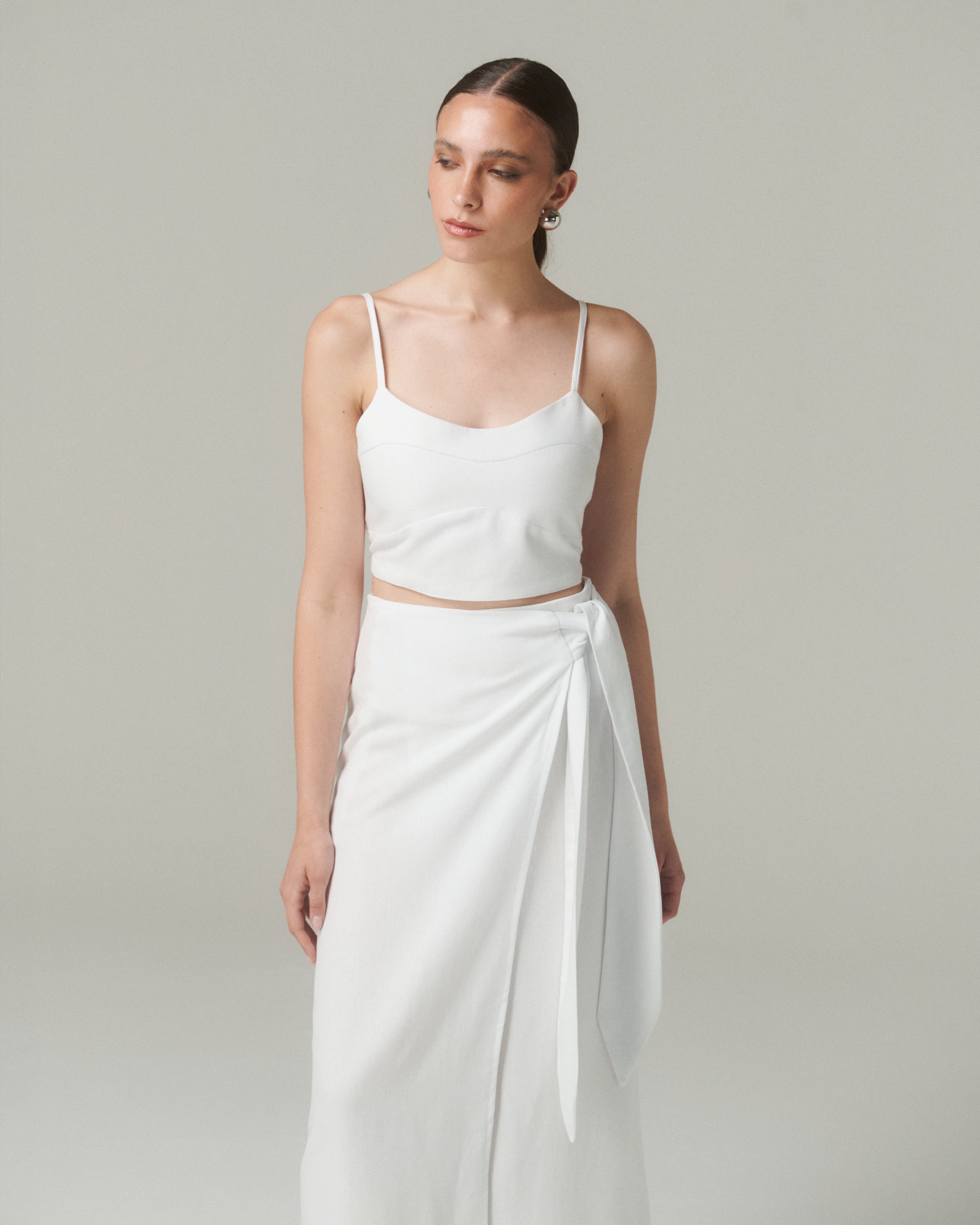 Modelo luciendo la Blusa Nina Blanco, una blusa blanca con tirantes finos y lazo ajustable en la espalda.