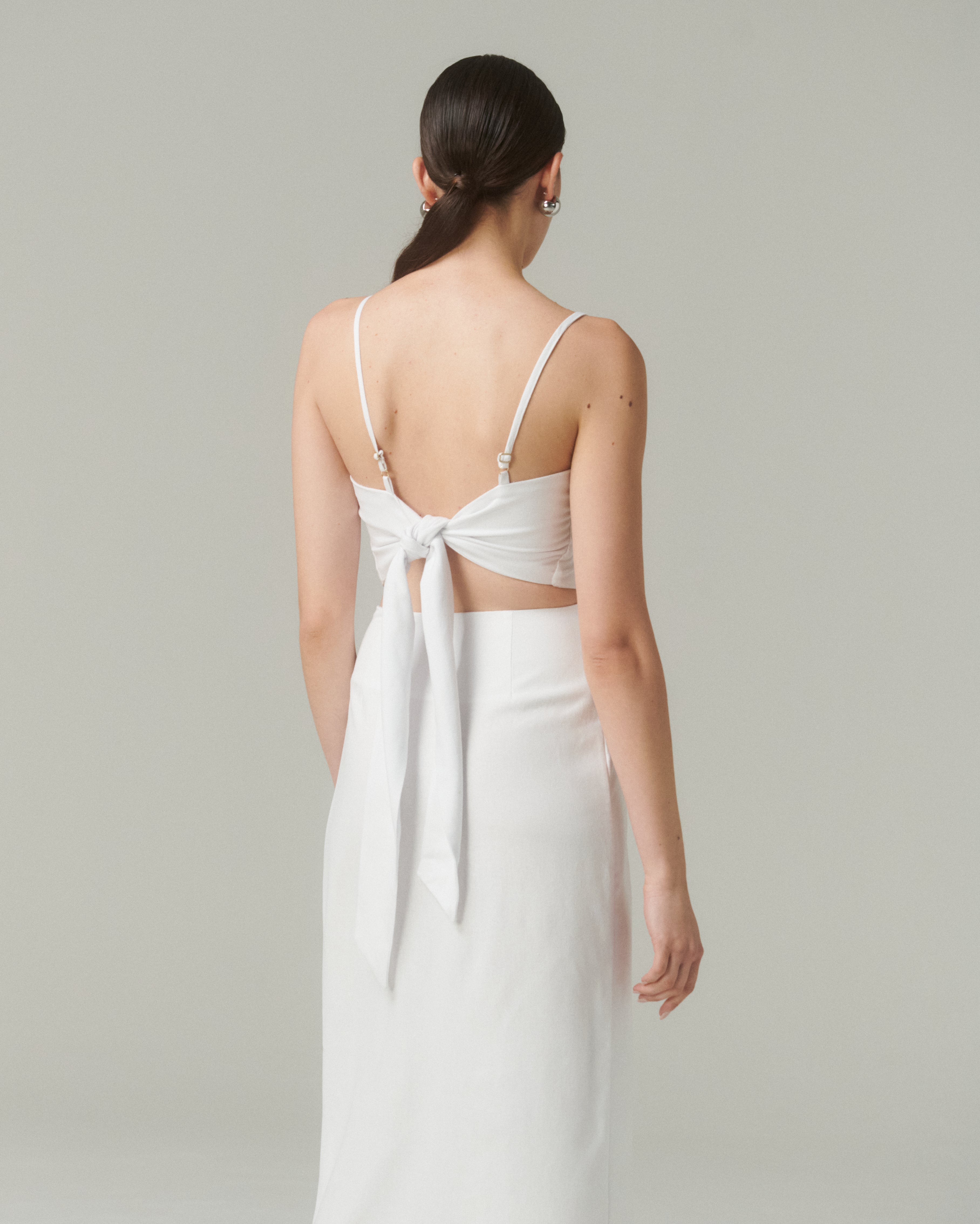 Blusa Nina Blanco, vista trasera con lazo ajustable y tirantes finos, diseño moderno y escote recto.